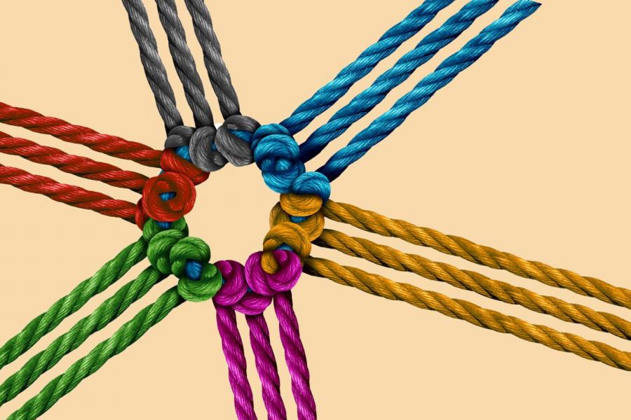 rappresentazione grafica stilizzata di un concetto di unità e connessione. Mostra otto corde colorate che si irradiano da un nodo centrale. Ogni corda è composta da tre fili intrecciati e ognuna ha un colore diverso: rosso, verde, grigio, blu, azzurro, giallo, arancione e viola.