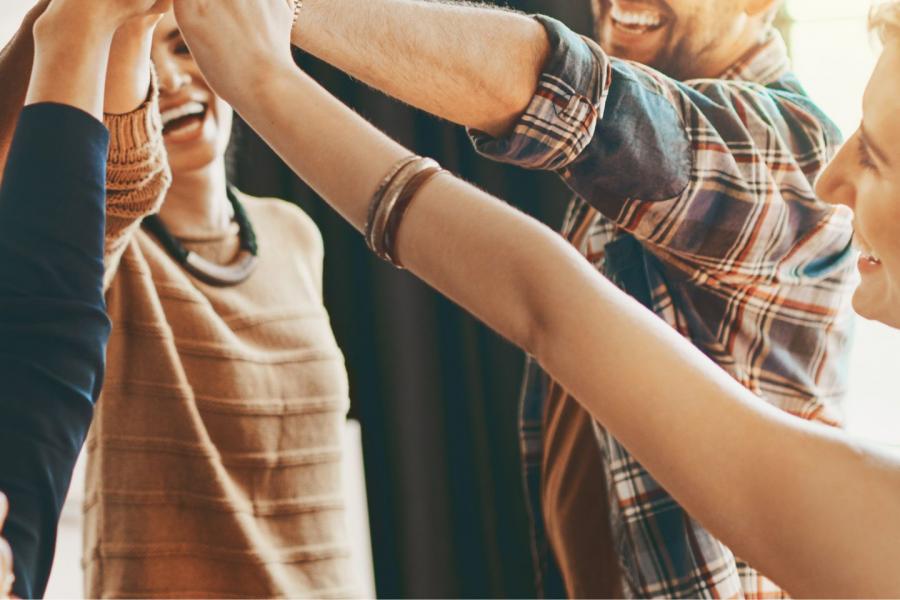 gruppo di giovani ragazzi e ragazze che si stanno "dando un cinque". Le mani di tutti si incontrano al centro in alto, i volti sono sfuocati sono in primo piano le mani unite