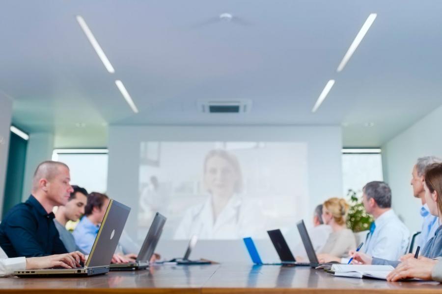 Una ripresa interna all'altezza degli occhi cattura un gruppo di professionisti, sia uomini che donne, seduti attorno a un grande tavolo da conferenza in legno lucido